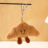 Smiling croissant plush bag charm with brown legs, a metal chain and keyring