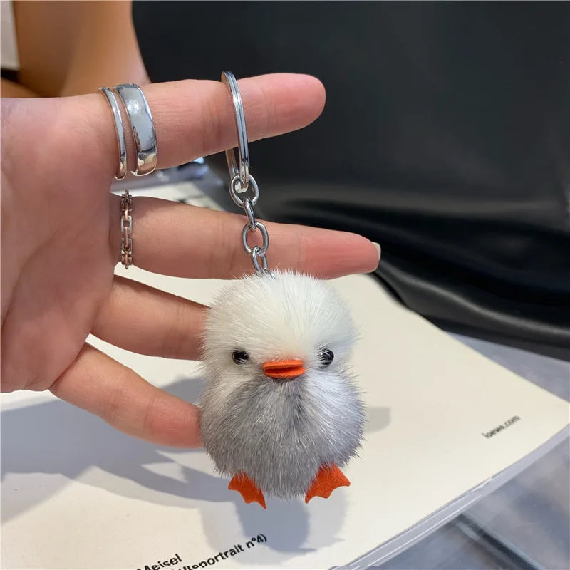 Gray-and-white fuzzy duck keychain with an orange beak and feet, a metal chain and keyring