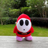 Red Shy Guy plush with white mask, black belt, and lavender feet