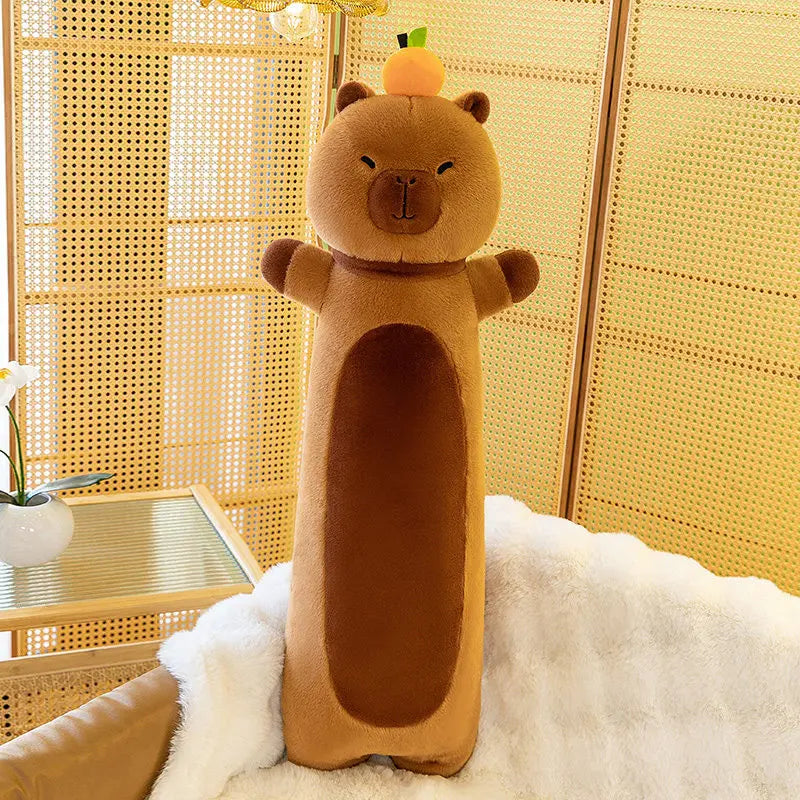 Long brown capybara plush body pillow with an orange on its head, standing against a woven screen