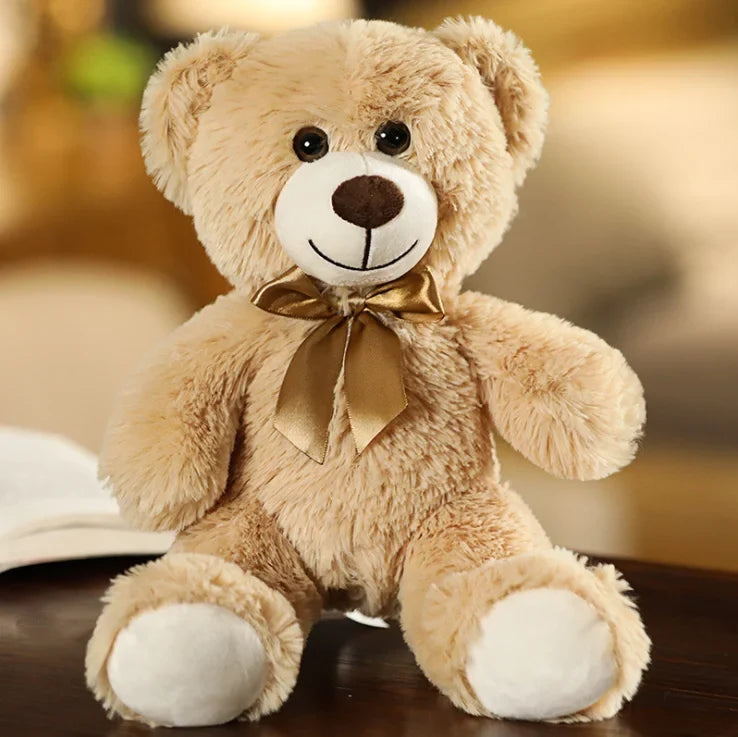 Beige teddy bear plush with a gold ribbon bow, cream muzzle and paw pads, and brown nose
