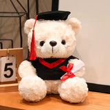 Cream graduation teddy bear with black cap and red trim, 25 cm