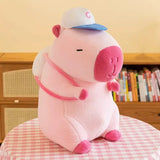 Pink capybara plush wearing a blue-and-white cap and small backpack with pink straps