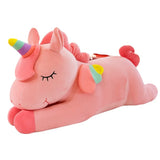 Pink sleeping unicorn plush with closed eyes, rainbow horn, and colorful wings