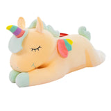 Yellow sleeping unicorn plush with closed eyes, rainbow horn, and colorful wings