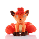 Orange Vulpix Pokémon plush with curled head fur, cream chest, brown paws, and curled tails